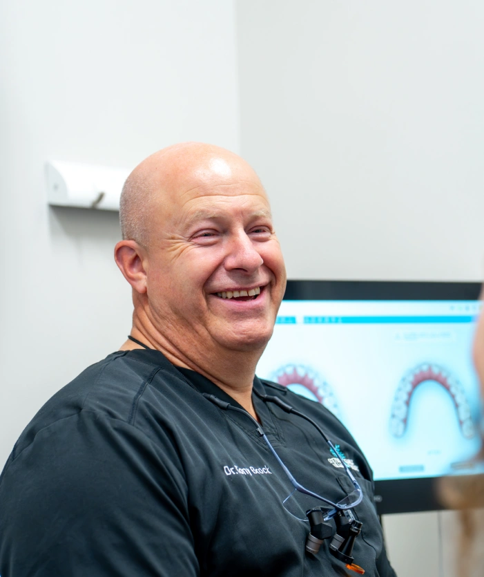 Dr. Tony Brock smiling with a patient, dental scan visible on screen behind him