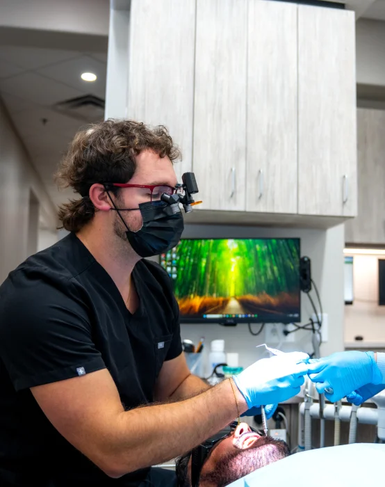Stetson Village Family Dentistry dentist in loupes performs a dental cleaning and exam on a patient
